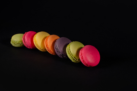 colored macaroons on a black background. red, yellow, pink, green, brown macaroon. Knit sweater, palm on a black background. A palette of bright colors, a stove, a dietary cookie. Elite bakingの写真素材