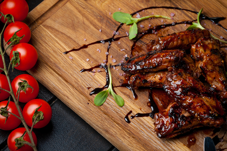chicken wings baked on fire with mustard sauce, valerian, cherry tomatoes and cream sauce on a wooden boardの写真素材