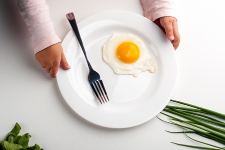 Children's hands hold a white plate with an egg, a fork and a knife. white background, photo from aboveの写真素材