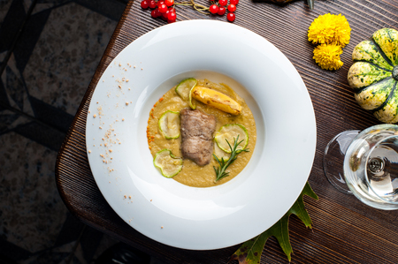 Pumpkin cream soup with fish som. A dish at a restaurant for Halloween celebrations. Black background, brick wall and wooden tableの写真素材