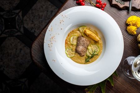 Pumpkin cream soup with fish som. A dish at a restaurant for Halloween celebrations. Black background, brick wall and wooden tableの写真素材