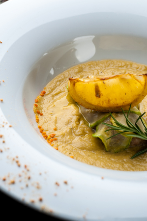 Pumpkin cream soup with fish som. A dish at a restaurant for Halloween celebrations. Black background, brick wall and wooden tableの写真素材