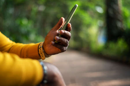 a person using a smartphone on green bokeh background, male hand holding a smartphoneの写真素材