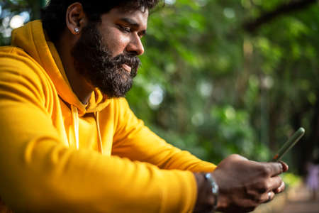 Man with a yellow outfit using a smartphone in a park, Indian male model with green background