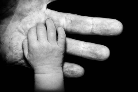 A black and white close up of a soft newborn baby's hand contrasted by his or her Father's gruff weathered hand の写真素材