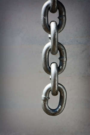 A detailed closeup macro of a heavy duty chain dangling in front of a dingy white wall.  Room for...