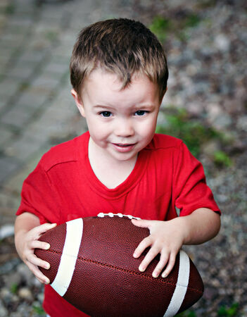 A small boy clutching a football looks hopefully at the viewer as if to say;  do you want to play  の写真素材