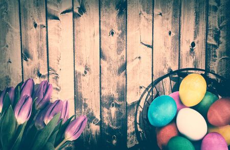 A bouquet of tulips and a wire basket full of Easter Eggs on top of a rustic wooden background...