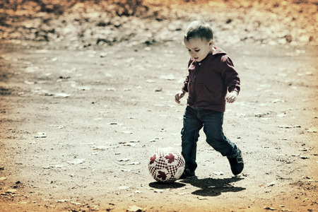 A small boy takes a kick at the soccer ball as he enjoys some time outdoors on a brisk early spring or late fall day   Processed for an vintage retro look の写真素材