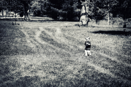 A young boy walks in a park holding and inspecting a dandelion flower.  Processed in black and white.の写真素材