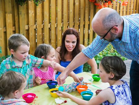 Family fun painting and decorating eggs outside during the spring season in a garden setting.  Father helps his children color dye their Easter eggs as the mother watches on.  Part of a series.の写真素材