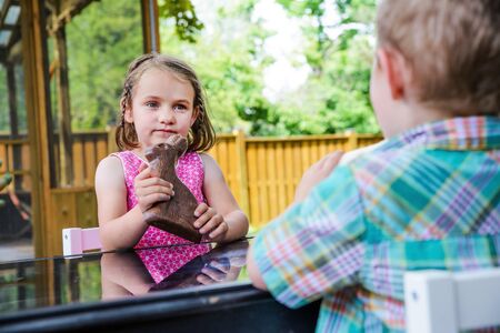 A little girl in a pink dress sits outside holding a large chocolate bunny on Easter day during the spring season.  Part of a series.の写真素材