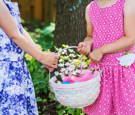 A close up of two little girls hands holding a basket with flowers and colorful dye decorated Easter...