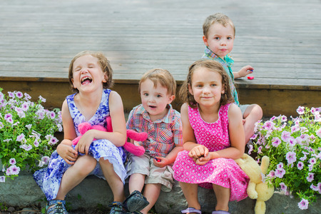 Two boys and two girls holding stuffed bunnies are having fun sitting outside in a garden eating...