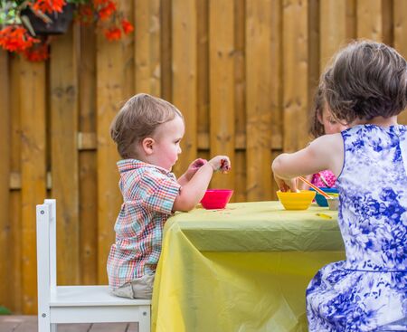 A small boy and a young girl sit outside at a crafts table color dyeing Easter eggs during the spring season in a beautiful garden setting.  Part of a series.の写真素材
