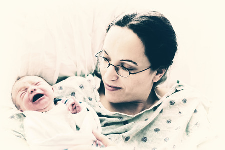 A new mother holds her crying newborn baby.  Filtered to give vintage, faded look.の写真素材