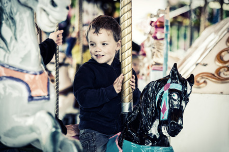 A happy young boy sits on a horse on a carousel ride in an amusement park.の写真素材
