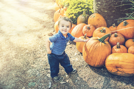 A young boy poses with his hand resting on a pumpkin he has picked at a farm during the autumn...