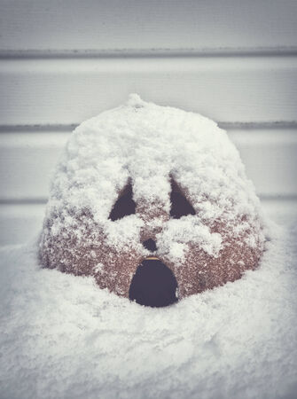 A jack o lantern pumpkin with a scared expression on its face sits outside covered in snow...