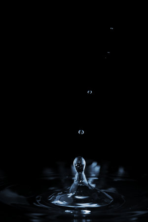 Splash and ripple on the clear water surface liquid from a falling drop. On a dark backgroundの写真素材