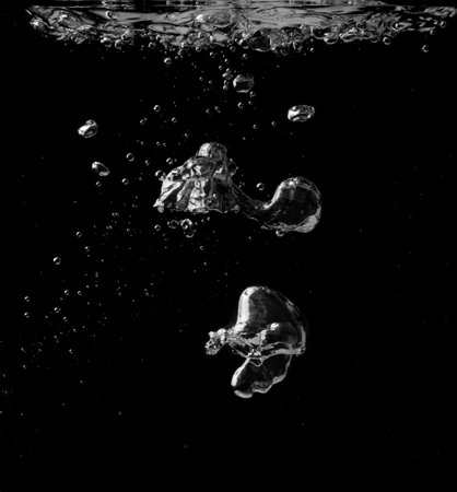 Splashing and bubbles on a clear water liquid surface. Isolated on a blackの写真素材