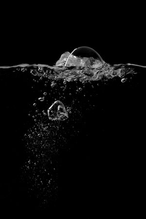 Splashing and bubbles on a clear water liquid surface. Isolated on a black