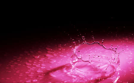 Beautiful splash crown from a drop of water falling on a hard surface. In red light on a black...