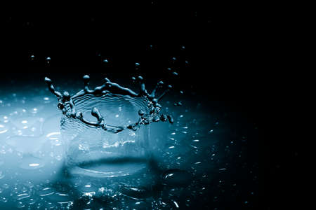 Beautiful splash crown from a drop of water falling on a hard surface. In blue light on a black backgroundの写真素材