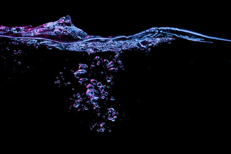 Clear water surface with ripple and bubbles in red and blue light on a black nature background