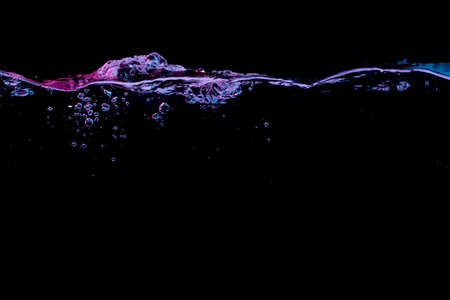 Clear water surface with ripple and bubbles in red and blue light on a black nature backgroundの写真素材
