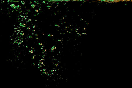 A bubble splash in transparent clear water liquid in green and yellow light on a black nature backgroundの写真素材