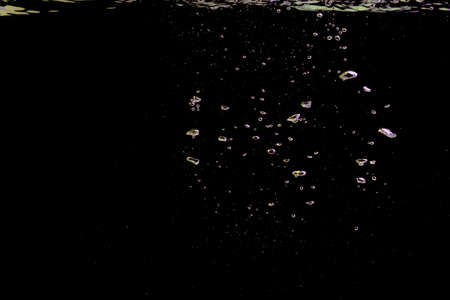 A bubble splash in transparent clear water liquid in yellow and purple light on a black nature backgroundの写真素材