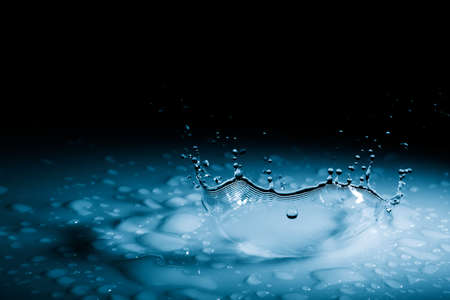 Beautiful splash crown from a drop of water falling on a hard surface. In blue light on a black backgroundの写真素材