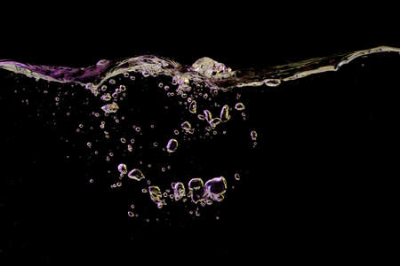 Clear water surface with ripple and bubbles in yellow and purple light on a black nature background