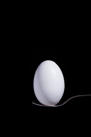 white egg on a spoon on a black background