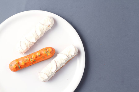 pumpkin orange eclair and white coconut eclairs on a white plate and grey tableの写真素材