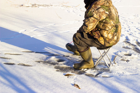 The fisherman sits at the ice hole waiting for the fishの写真素材