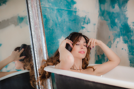 Pretty brunette woman taking a bath and listen music in headphonesの写真素材