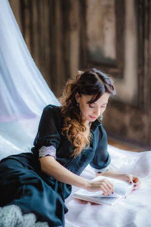 Portrait of pretty brunette model lies on bed with canopy and reading a bookの写真素材
