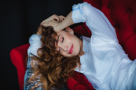 pretty brunette young woman posing on red sofaの写真素材