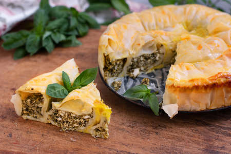 Spiral pie made of filo dough, spinach and feta cheese on wooden background. Authentic Greek bakery.の写真素材