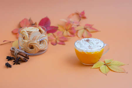 Pumpkin spice latte in a glass mug with whipped cream on beige background. Autumn leaves. Hot autumn drink.の写真素材