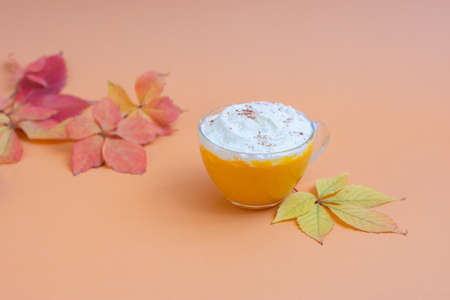 Pumpkin spice latte in a glass mug with whipped cream on beige background. Autumn leaves. Hot autumn drink.の写真素材