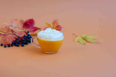 Pumpkin spice latte in a glass mug with whipped cream on beige background. Autumn leaves. Hot autumn drink.の写真素材