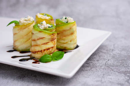 Zucchini appetizer rolls with cream cheese and basil on white plate on gray background. Fried vegetable marrow sushi rolls. Fried zucchini.の写真素材