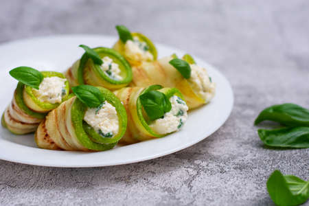Zucchini appetizer rolls with cream cheese and basil on white plate on gray background. Fried vegetable marrow sushi rolls. Fried zucchini.の写真素材