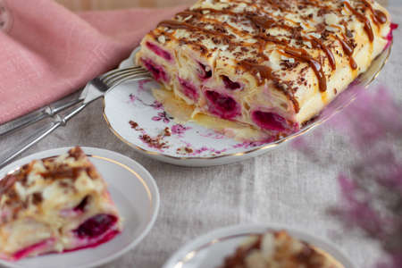 Cake from rolled pancakes with custard, cherries and grated chocolate on white plate, on a light background.の写真素材