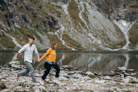 Girl in yellow sweater holding boy's hand and running high in the mountains.  Breathtaking view.の写真素材