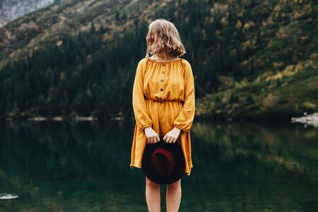 Magnetic girl in the yellow dress with red hat in her hands by stunning lake Morskie oko in mountainsの写真素材