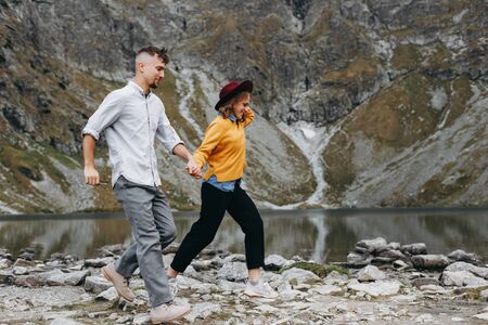 Girl in yellow sweater holding boy's hand and running high in the mountains.  Breathtaking view.の写真素材